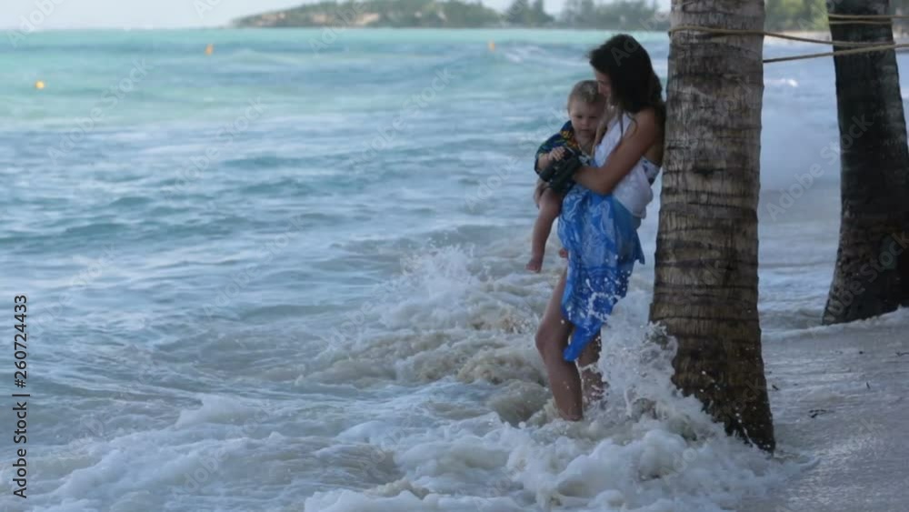 Mom and toddler boy, happily hugging on the ocean shore, relaxing and enjoying the waves Mom and toddler boy, happily hugging on the ocean shore, relaxing and enjoying the waves