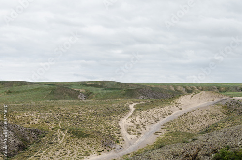 Automobile dirt and dusty roads among green hills and rocks in the mountainous region of Kazakhstan.