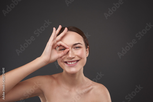 Cheerful young woman encircling her eye with fingers