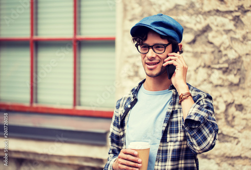 leisure, technology, communication and people concept - hipster man in eyeglasses calling on smartphone and drinking coffee on street