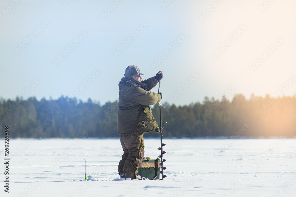 a man on a winter fishing drill hole ice drill