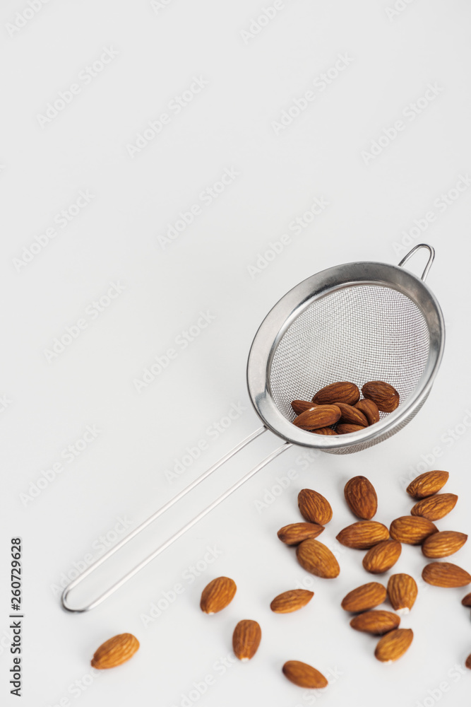 Fototapeta premium scattered almonds and sieve on grey background with copy space