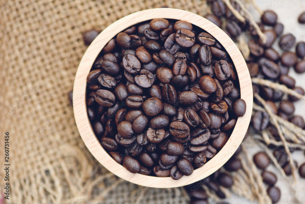 Fototapeta premium Roasted coffee beans in sack background / Closeup macro of coffee beans on wooden bowl - top view