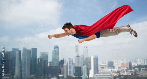 super power and people concept - happy young man in red superhero cape flying in air over singapore city skyscrapers background