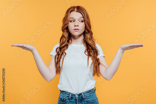 beautiful redhead girl showing shrug gesture isolated on yellow