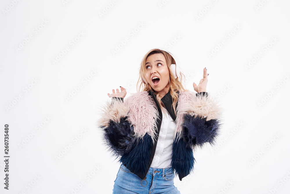beautiful redhead woman in fur coat and white headphones listens to music and dancing on white isolated background beautiful redhead woman in fur coat and white headphones listens to music and dancing on white isolated background