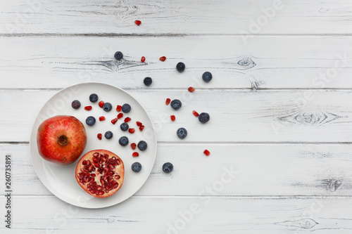 blueberries and pomegranate on a plate on distressed white wood