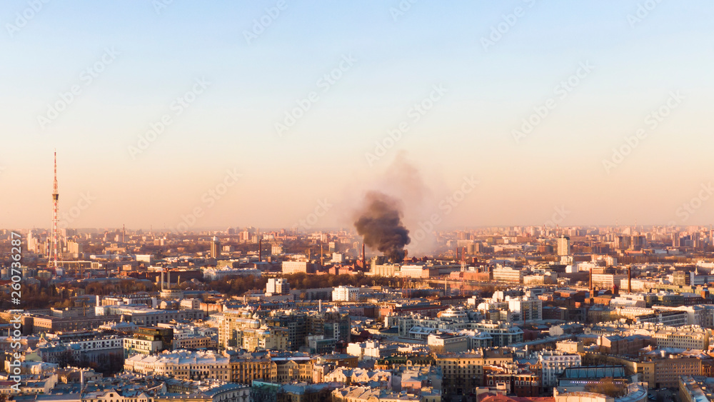 Black smoke rises above the horizon in the city, the building burns. Aerial view at sunset