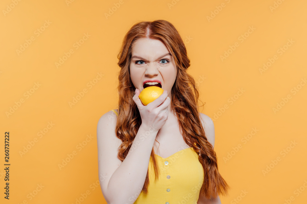 redhead girl looking at camera, making facial expression and biting lemon isolated on yellow redhead girl looking at camera, making facial expression and biting lemon isolated on yellow