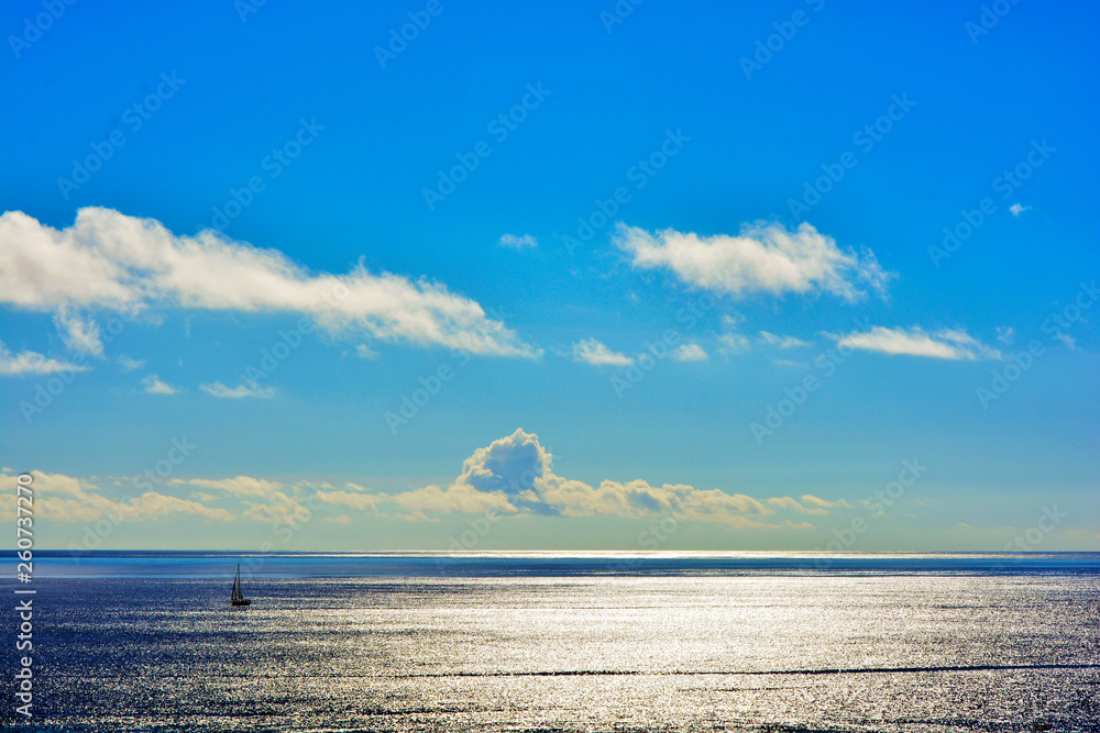 Lonely sailboat in the ocean against the sky with the setting sun in the clouds