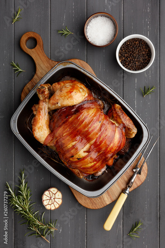 roast chicken in a rasting tin with ingredients and carving fork on dark grey wood