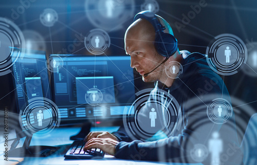 cybercrime, hacking and technology concept - male hacker in headset with progress loading bar on computer screen wiretapping or using virus program for cyber attack in dark room