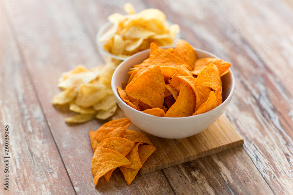 fast food, junk-food, cuisine and eating concept - close up of crunchy potato and corn crisps or nachos in bowls on wooden table