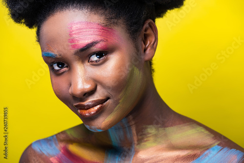 Smiling african american woman with bright makeup looking at camera isolated on yellow