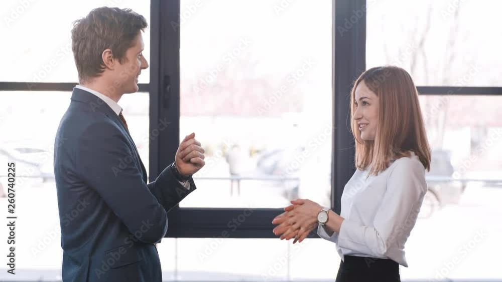 handsome man standing with crossed arms and talking with attractive and cheerful coworker while gesturing in office handsome man standing with crossed arms and talking with attractive and cheerful coworker while gesturing in office