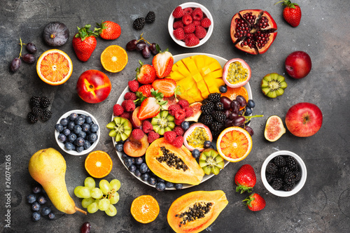 Fototapeta Naklejka Na Ścianę i Meble -  Delicious fruit platter mango pomegranate raspberries papaya oranges passion fruits berries on oval serving plate on dark concrete background, selective focus, top view