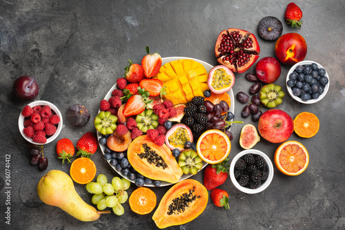 Delicious fruit platter mango pomegranate raspberries papaya oranges passion fruits berries on oval serving plate on dark concrete background, selective focus, top view, copy space