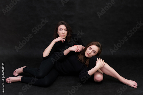 Concept portrait of two stylish brunette sisters on a black background in various poses. Fashionable photo of two beautiful girls with dark hair