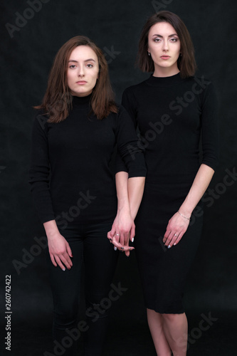 Concept portrait of two stylish brunette sisters on a black background in various poses. Fashionable photo of two beautiful girls with dark hair