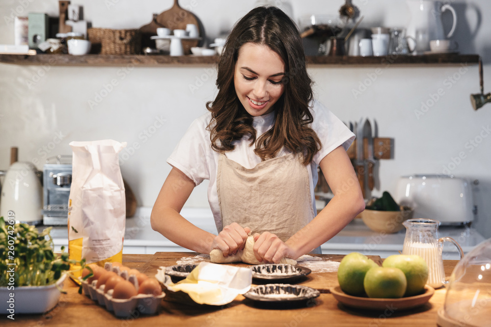 Cheerful young woman wearing apron preparing dough