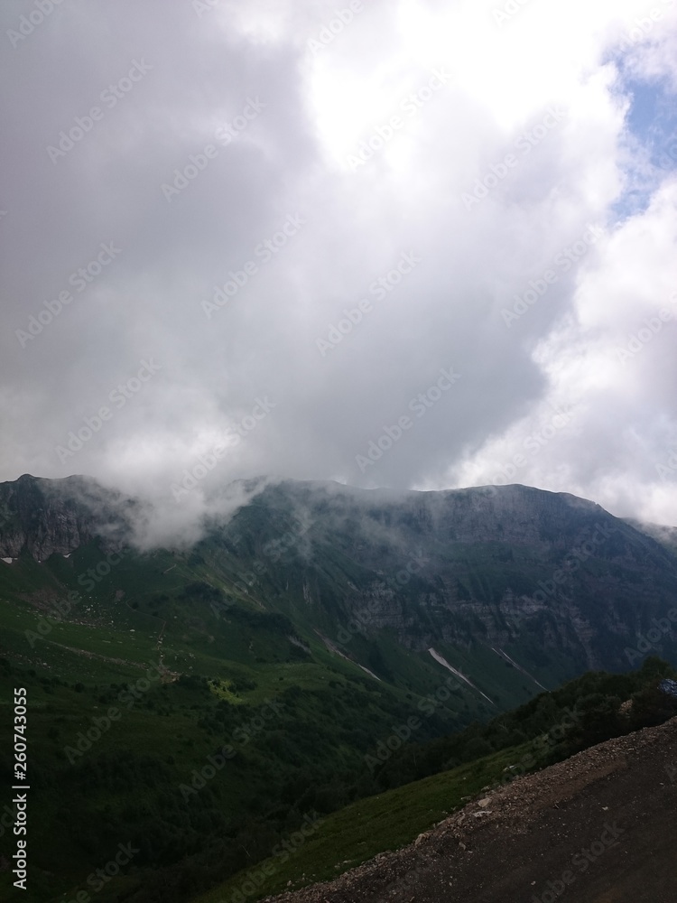 Mountain slope with cable cars and ski slopes on a cloudy summer day, fog, clouds. Black Pyramid Mountain, Krasnaya Polyana, Sochi, Caucasus, Russia.