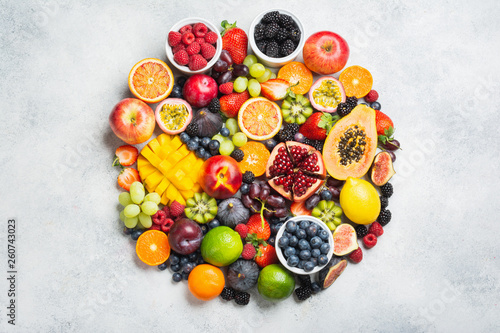 Circle made of healthy raw rainbow fruits, mango papaya strawberries oranges passion fruits berries on oval serving plate on light concrete background, top view, copy space, selective focus