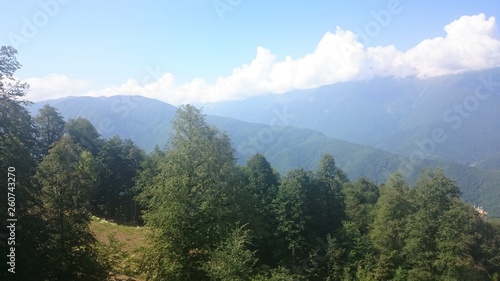 The tops of the high mountain slope of the black pyramid  with a cable car in front of which is the valley. Blue sky in the mountains on a summer day. Krasnaya Polyana  Sochi  Russia.