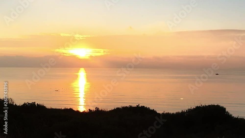Sunset over sea with seagulls and fishing boat on the horizon.