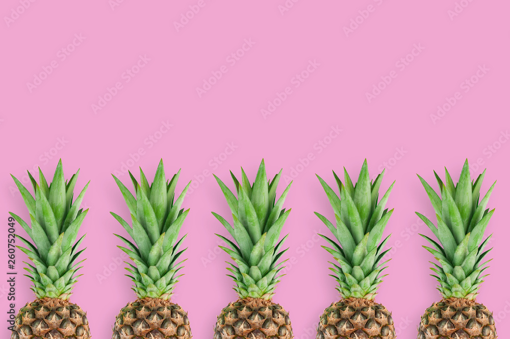 Fototapeta premium Row of fresh pineapples with green leaves lying on pink table on kitchen. Top view. Cooking concept