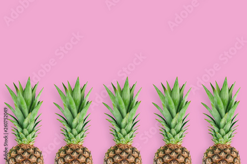 Row of fresh pineapples with green leaves lying on pink table on kitchen. Top view. Cooking concept