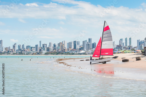 Carrying a sailing boat on a beach. Praia do Bessa beach, Joao Pessoa PB, Brazil. Beachfront buildings on background.