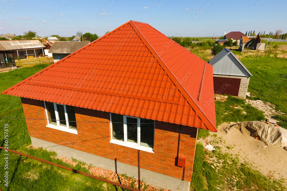 House with an orange roof made of metal, top view. Metallic profile painted corrugated on the roof. House with an orange roof made of metal, top view. Metallic profile painted corrugated on the roof.