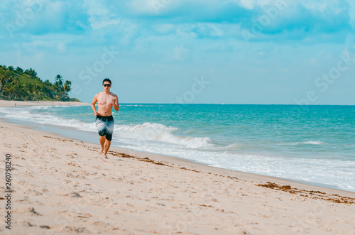 Man running on the beach during summer. Doing cardio exercise on the sand. Photo at Praia de Tabatinga 2, Conde PB Brazil. 