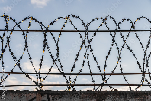 The black shabby barbed metal wire on wires on a fence against a blue sky