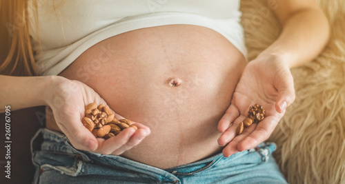 Happy pregnant woman at home eating fresh nuts - almonds, walnuts. Healthy pregnancy concept.