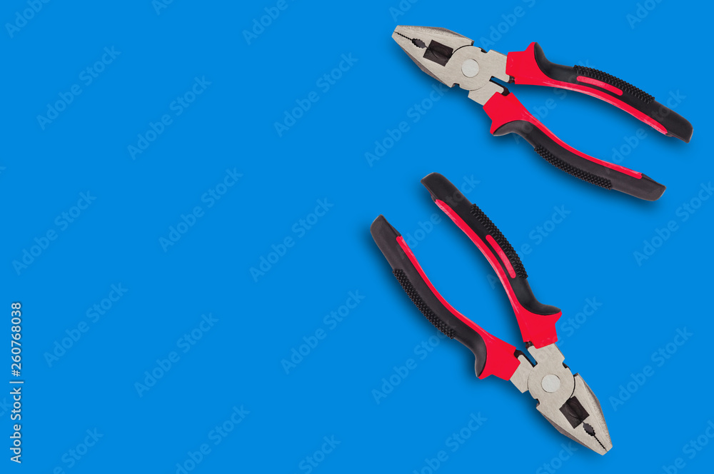 Two new metal pliers with rubber handles black and red color on blue table with copy space for your text. Top view. Repair or building concept Two new metal pliers with rubber handles black and red color on blue table with copy space for your text. Top view. Repair or building concept