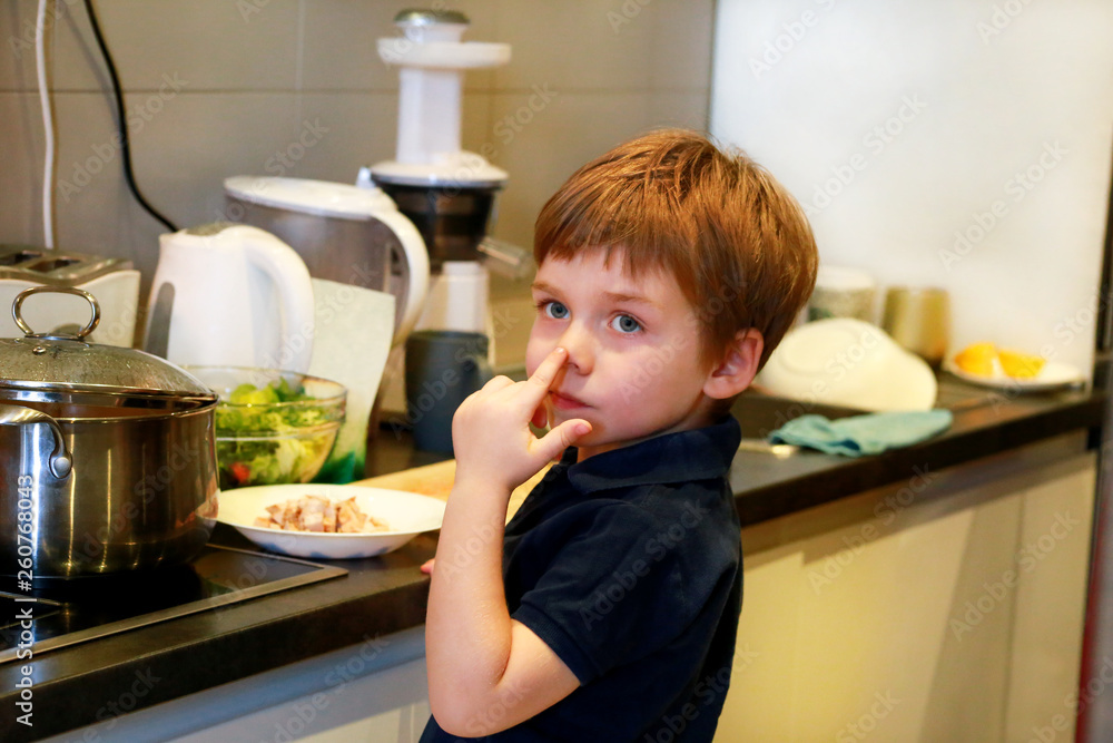 Portrait of child in kitchen. Cute little boy, playing in kitchen. Young kid is hungry, looks at and checks is it finished lunch. Childhood, food and drink concept. Education, fun, leisure, happiness. Portrait of child in kitchen. Cute little boy, playing in kitchen. Young kid is hungry, looks at and checks is it finished lunch. Childhood, food and drink concept. Education, fun, leisure, happiness.