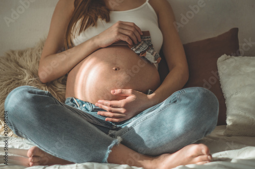 Tableau sur toile Beautiful pregnant woman holds small child clothes