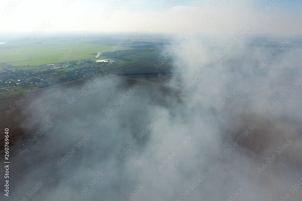 Fototapeta premium The smoke over the village. Clubs of smoke over the village houses and fields. Aerophotographing areas