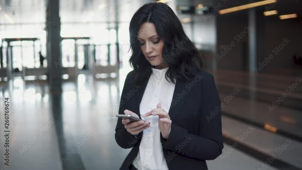 a woman in a business suit walks through the lobby of a modern office building. business woman uses a mobile phone. a woman in a business suit walks through the lobby of a modern office building. business woman uses a mobile phone.