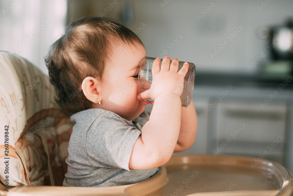 Cute little girl sitting in baby chair and drinking water Cute little girl sitting in baby chair and drinking water