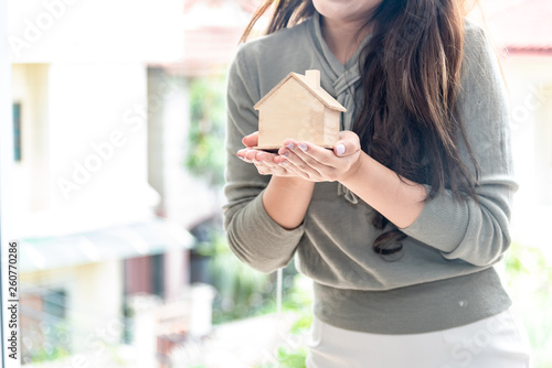 Happiness smiley woman holding small wooden mockup home model in hand. Mortgage property insurance and business real estate concept.