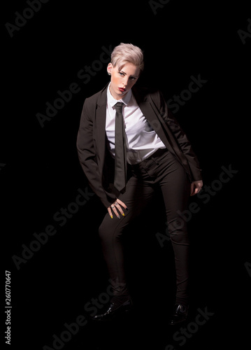 Short haired blonde woman wearing a suit, shirt and tie on a black background © Cian