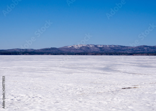 Winter landscape  frozen lake under snow and mountains on a skyline. Blue sky  sunny cloudless day.