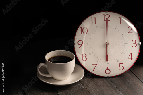 Coffee cup and clock on black wooden background.