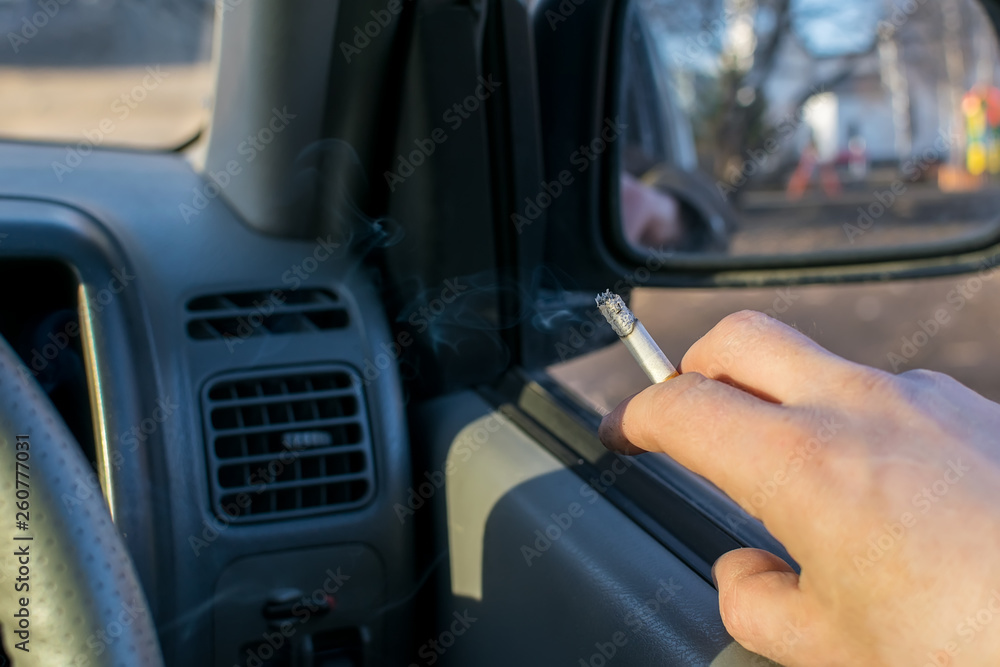 close-up, male hand holding a cigarette in a car that stands on the parking lot in a residential area