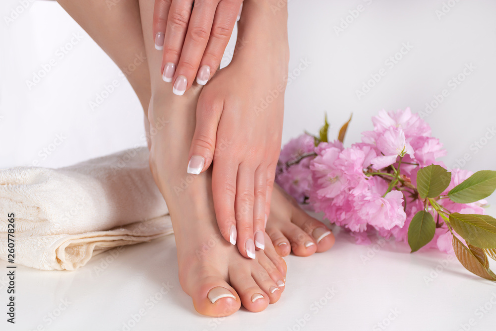 Beautiful female bare feet and hands with french manicure and pedicure on white towel in studio and pink decorative flower in background. Nails polish concept. Close up, selective focus Beautiful female bare feet and hands with french manicure and pedicure on white towel in studio and pink decorative flower in background. Nails polish concept. Close up, selective focus