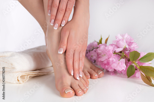 Beautiful female bare feet and hands with french manicure and pedicure on white towel in studio and pink decorative flower in background. Nails polish concept. Close up, selective focus