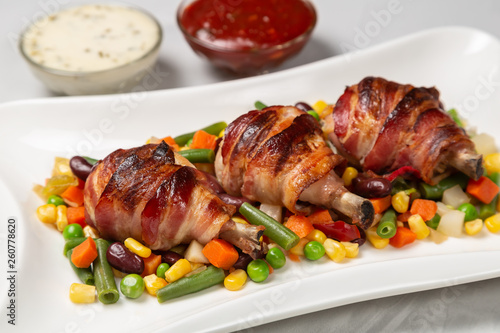 Fried chicken legs wrapped in bacon with vegetables
