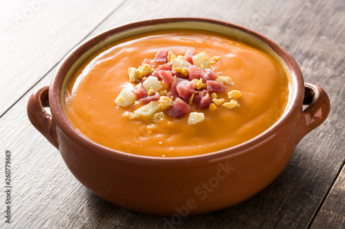 Typical Spanish salmorejo cream with ham and egg on wooden table. 